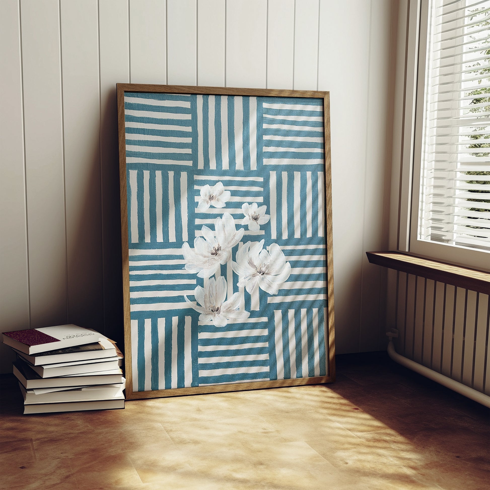 Framed artwork with floral design on a wall next to a stack of books.