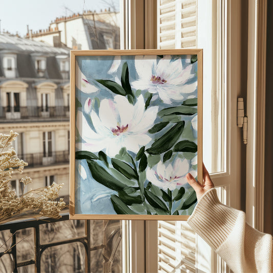 Framed floral artwork held by a person in front of a window with cityscape view