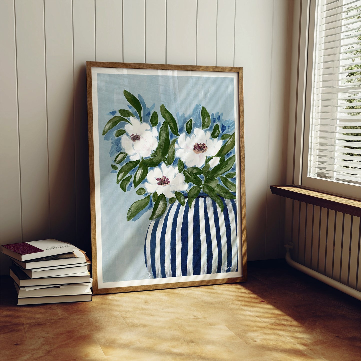 Framed artwork of flowers in a striped vase on a wooden floor.