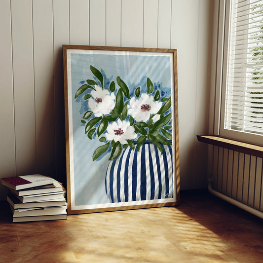Framed artwork of flowers in a striped vase on a wooden floor.