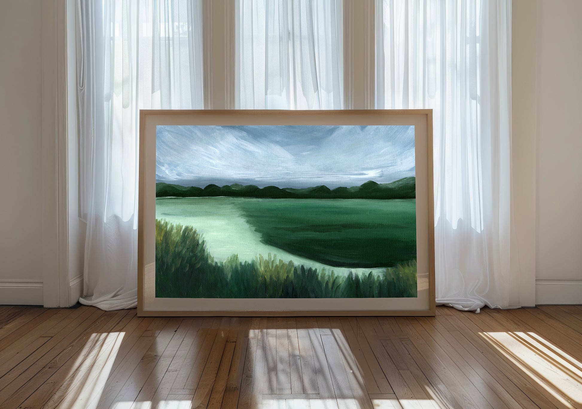 Framed landscape painting on a wooden floor with white curtains in the background