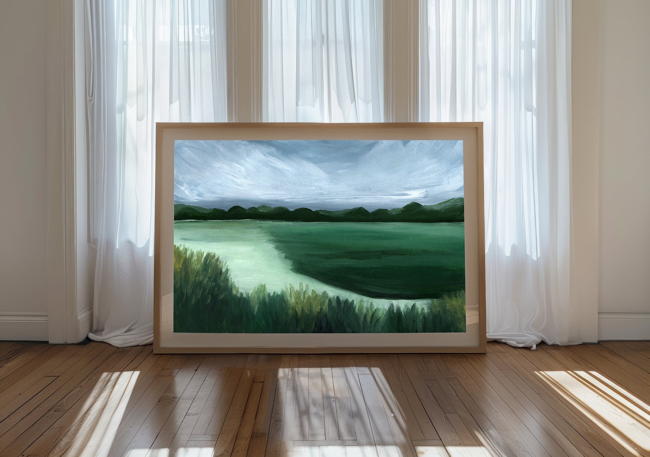 Framed landscape painting on a wooden floor with white curtains in the background