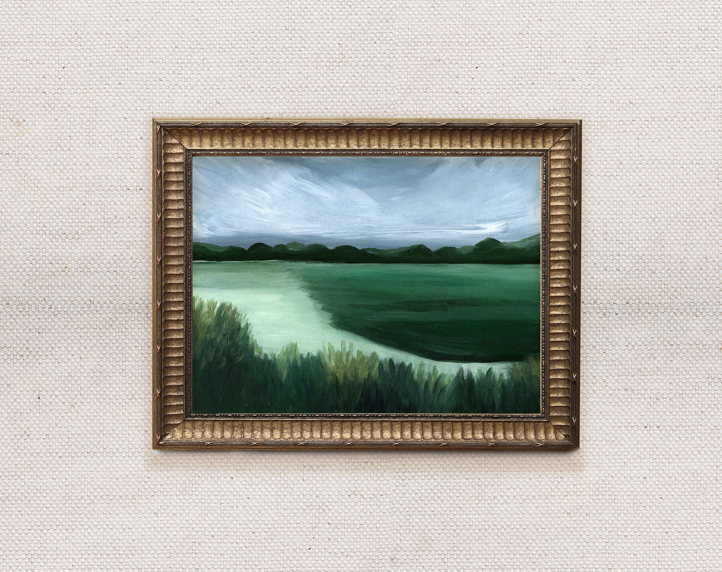 Framed painting of a landscape with green fields and trees on a textured wall.
