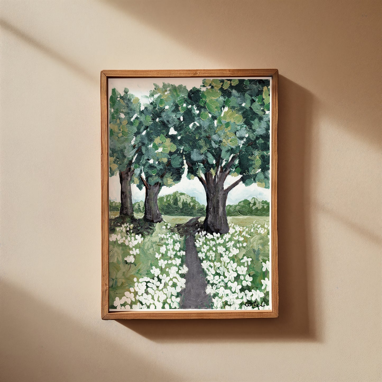 Framed painting of a landscape with trees and flowers on a beige wall.