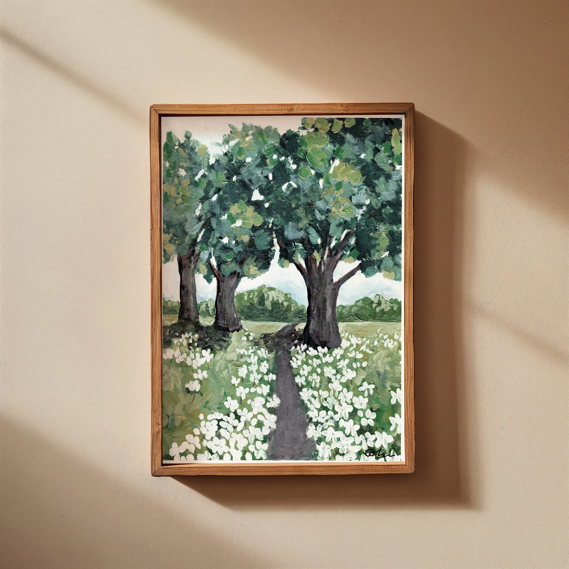 Framed painting of a landscape with trees and flowers on a beige wall.